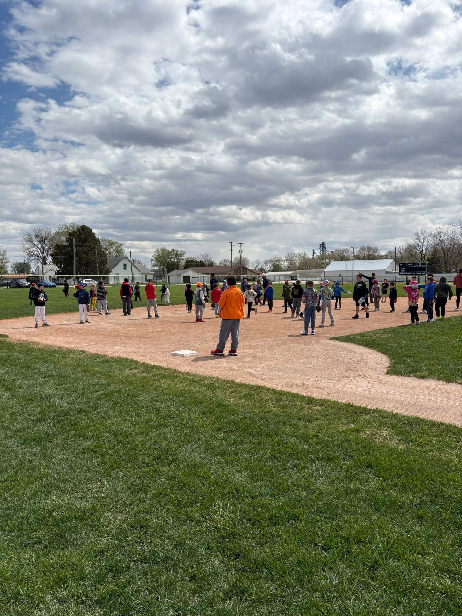 A coach in an orange jacket leading practice near second base