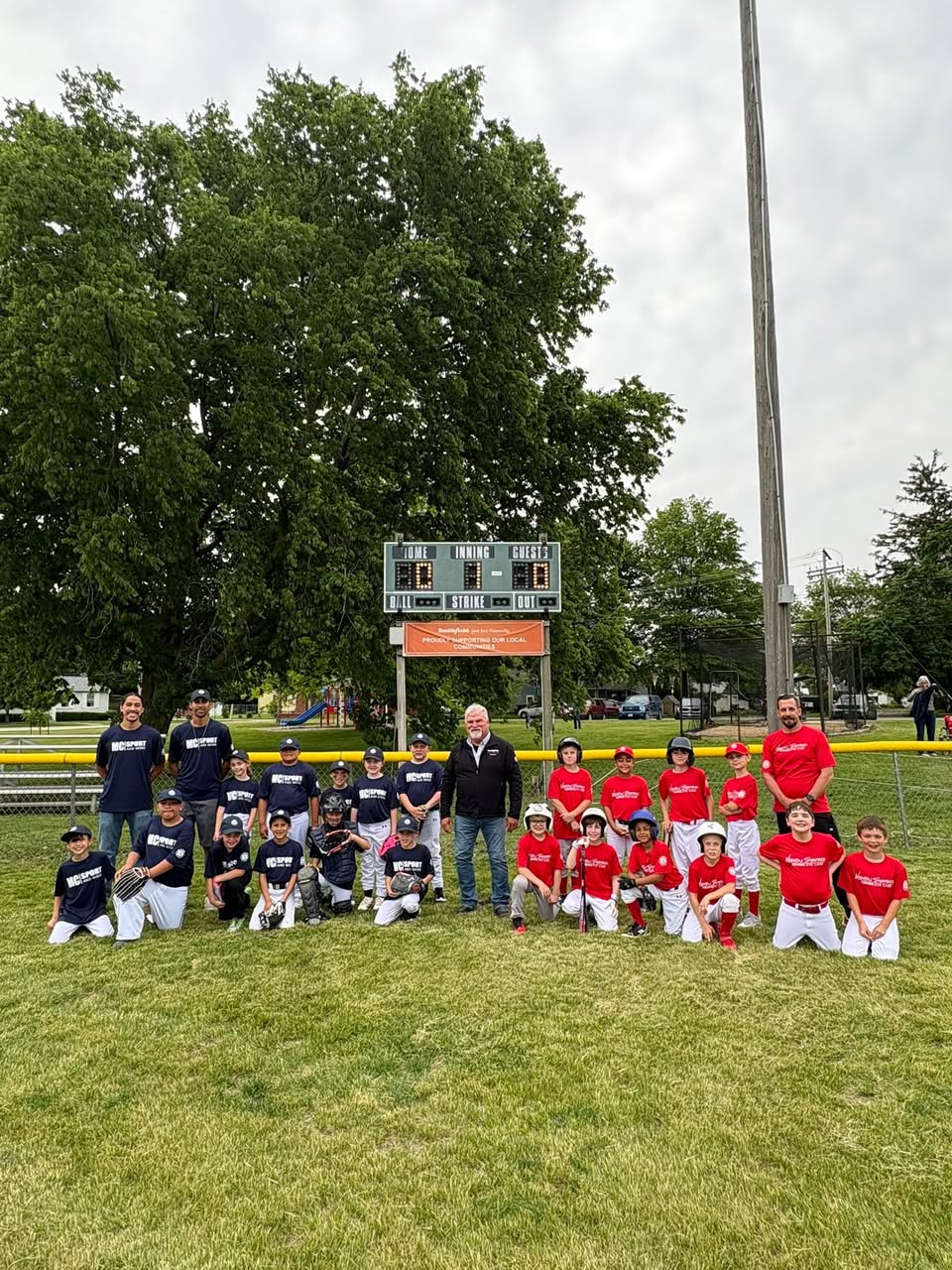 Two Monmouth Little Lions teams and their coaches posed together on the field in front of the scoreboard